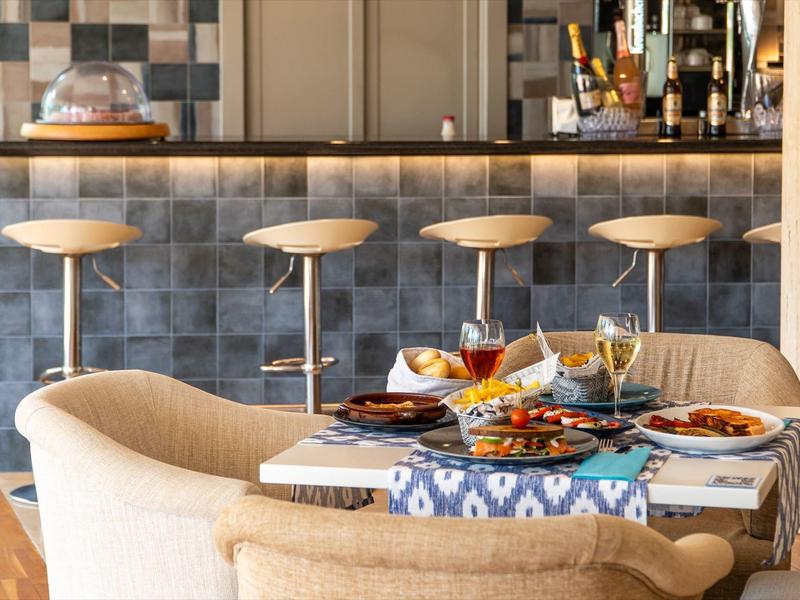 Elegancki stół do jadalni z jedzeniem i napojami przed barem z wysokimi stołkami we współczesnym wnętrzu.