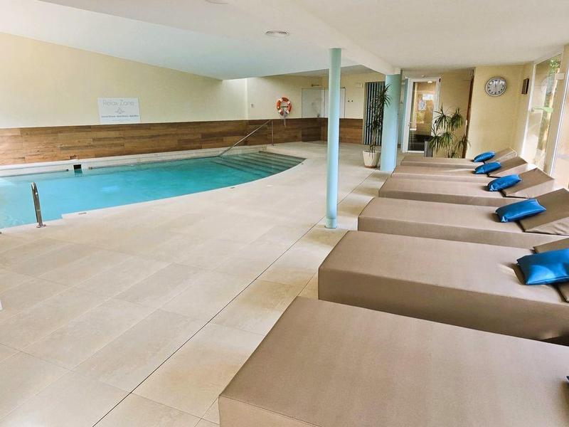 Wnętrze z basenem i leżakami z niebieskimi poduszkami w jasnej strefie spa.