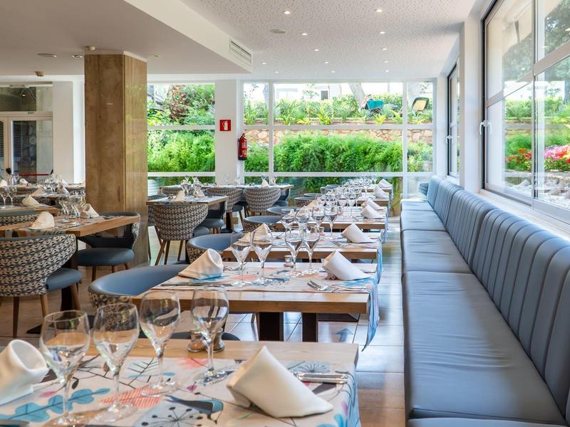 Jasna część restauracyjna z stołami, krzesłami i dużym oknem z widokiem na ogród.