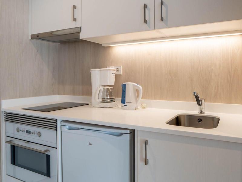 Mała kuchnia z kuchenką, lodówką, ekspresem do kawy i zlewem w białym kolorze.