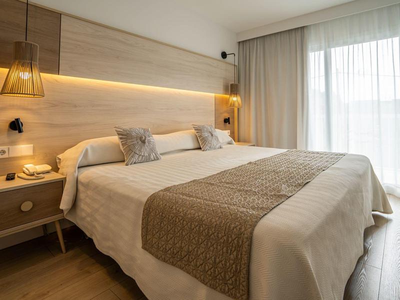 Nowoczesny pokój hotelowy z dużym łóżkiem, szafką nocną i oknem od podłogi do sufitu z zasłonami.