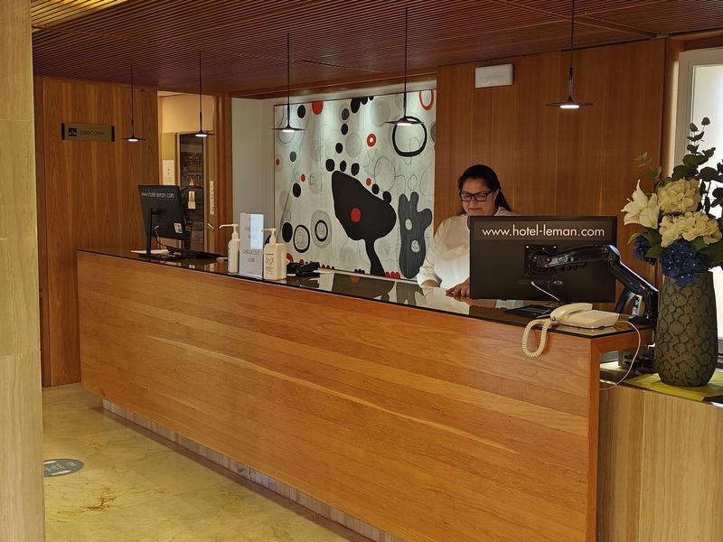 Recepcja hotelowa z drewnianymi panelami, komputerami i osobą za ladą.