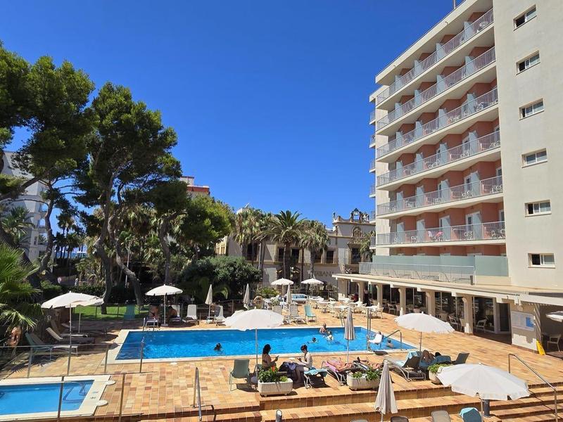 Hotel z dużym basenem na zewnątrz otoczonym leżakami i parasolami pod błękitnym niebem.