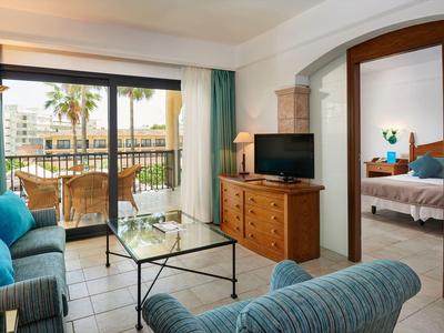 Gezellige hotelkamer met zithoek, glazen tafel, tv en balkon met uitzicht op palmbomen.