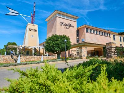 Gebäude mit Windmühle, braune Fassade und grüner Bepflanzung unter blauem Himmel.