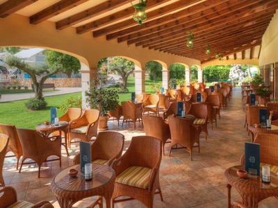Overdekt buitenterras met rieten stoelen en tafels met uitzicht op een groene tuin.