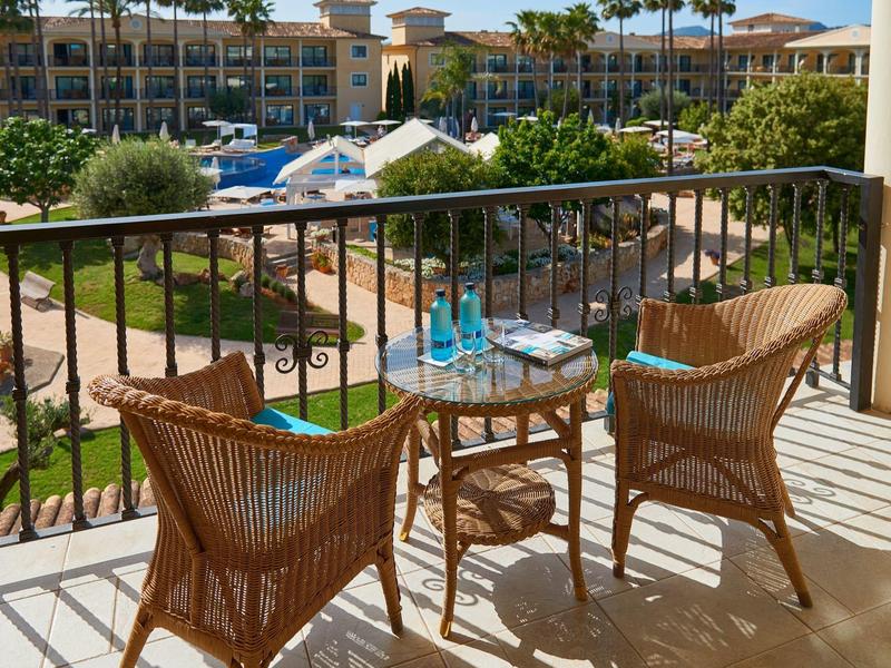 Balkon met twee rotan stoelen en tafel met uitzicht op een zwembad en hoteltuin.