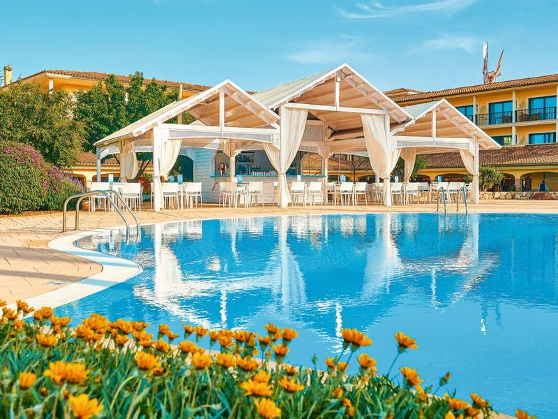 Cabana's met witte gordijnen en ligstoelen naast een helder blauw zwembad bij een resort.