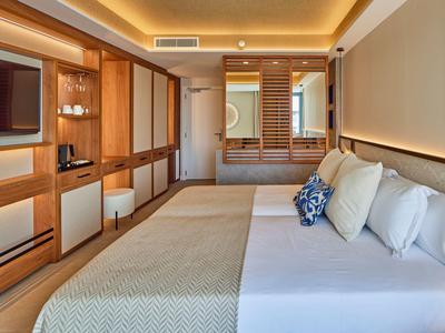 Modern hotel room with wooden furniture, large bed, and warm ambient lighting.