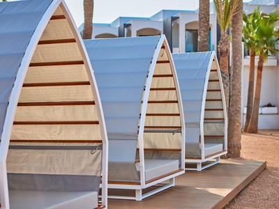 Three blue and beige outdoor cabanas with curved roofs by a sandy area and palm trees.