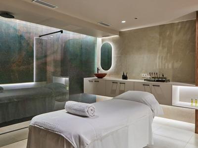 Modern spa room with massage table, rolled towel, bathtub, and ambient lighting.