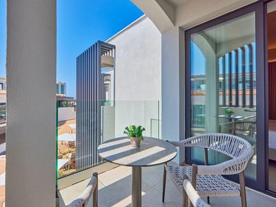 Modern balcony with table, chairs, glass railing, and view of neighboring buildings.