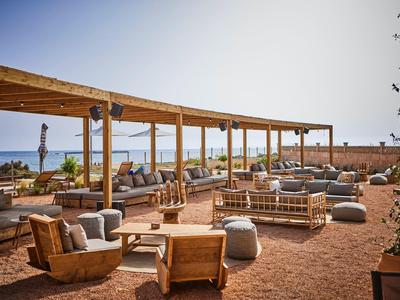 Outdoor seating area with wooden furniture and ocean view under a pergola at a sunny resort.