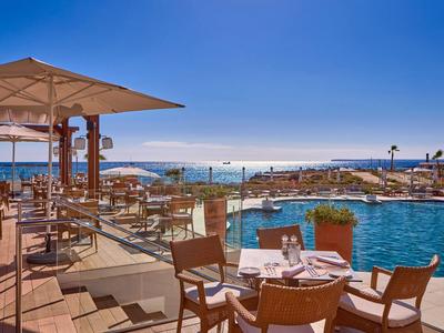 Outdoor hotel dining area beside pool with ocean views under clear blue sky.