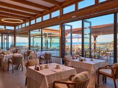 Cozy beachfront restaurant with wooden furniture and large windows overlooking the sea and umbrellas.