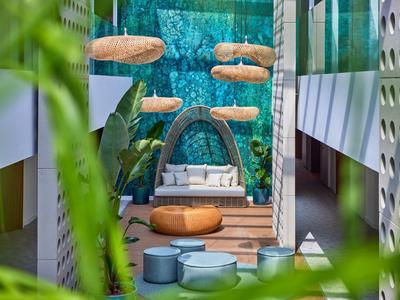 Modern outdoor lounge area with hanging seats, round ottomans, and a blue mosaic wall.