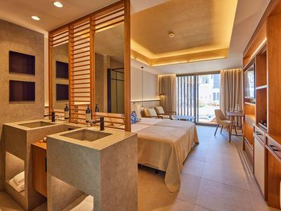 Modern hotel room with double bed, elegant lighting, open bathroom, and balcony with large windows.
