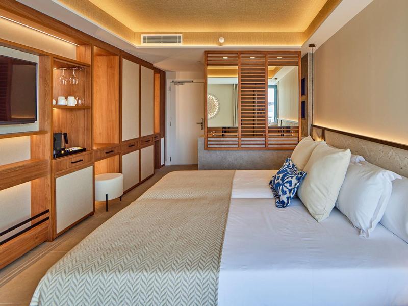 Modern hotel room with wooden furniture, large bed, and warm ambient lighting.