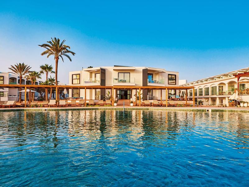 Resort with clear blue pool and palm trees under a bright sky.