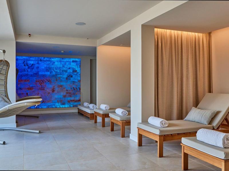Modern spa room with lounge chairs, white towels, and a calming blue water feature.