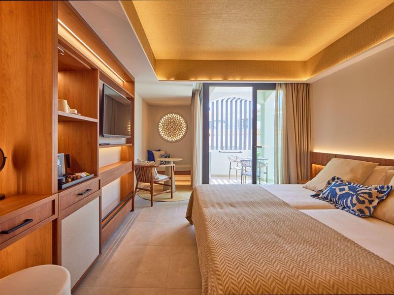 Modern hotel room with wooden furniture, a large bed, and balcony with city view.