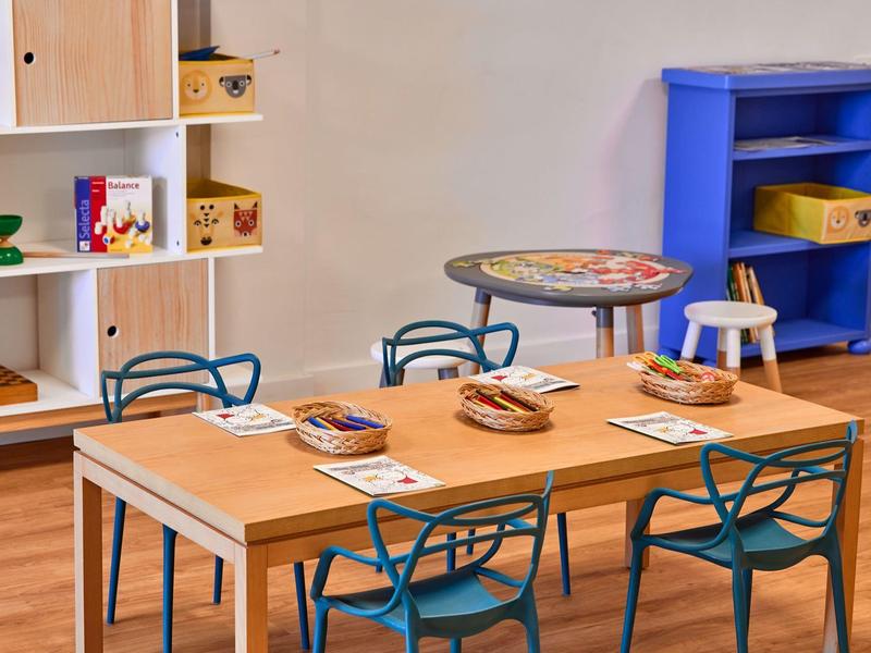 Cozy dining area with wooden table, teal chairs, and shelves against beige wall.