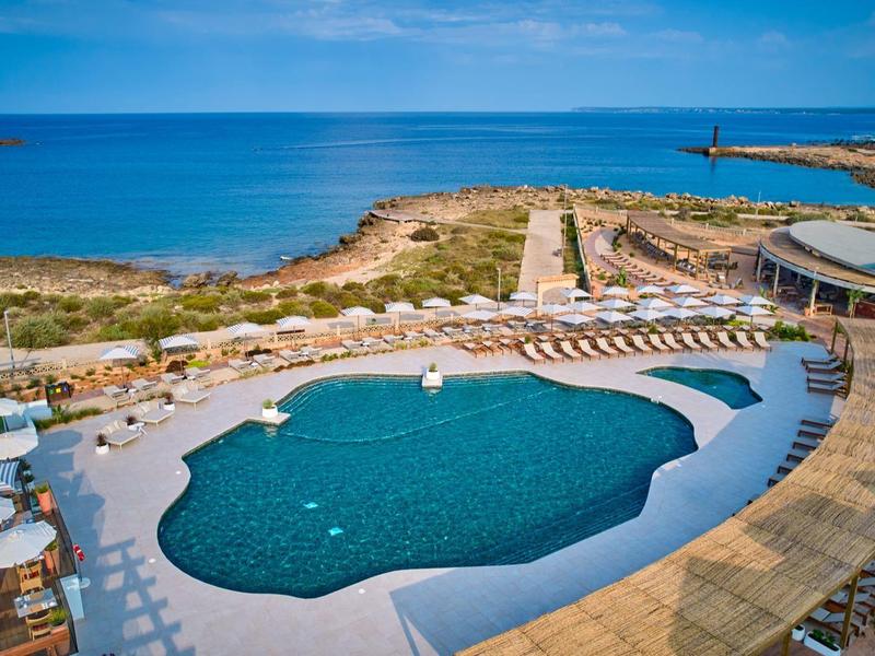 Curved outdoor pool with sun loungers overlooking the ocean on a clear day.
