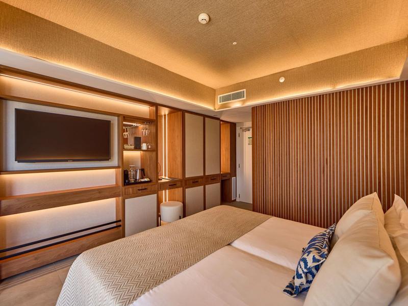 Modern hotel room with double bed, wooden panel accents, and ambient lighting.