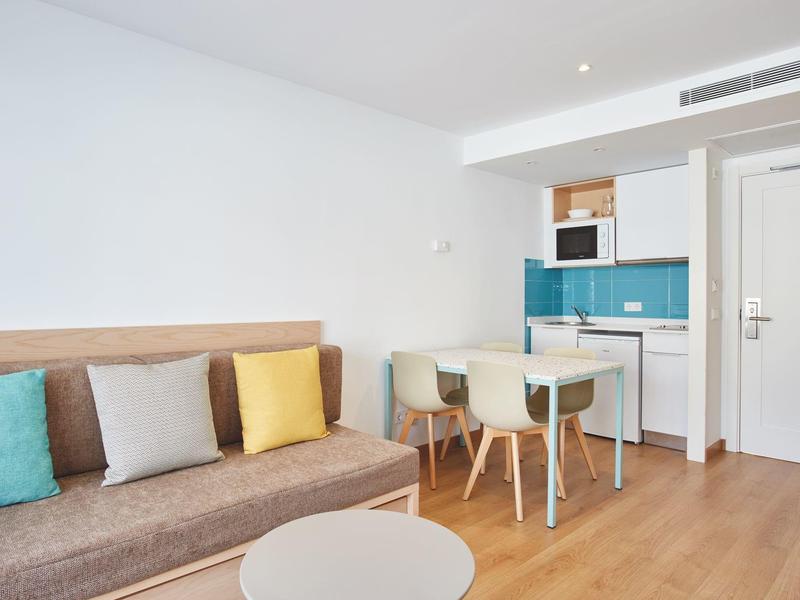 Zona giorno moderna con divano marrone, cuscini colorati, tavolo da pranzo e angolo cottura.