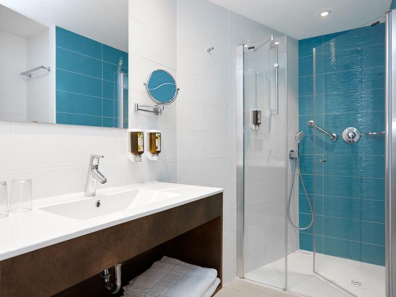 Bagno moderno con cabina doccia in vetro e pareti piastrellate blu.