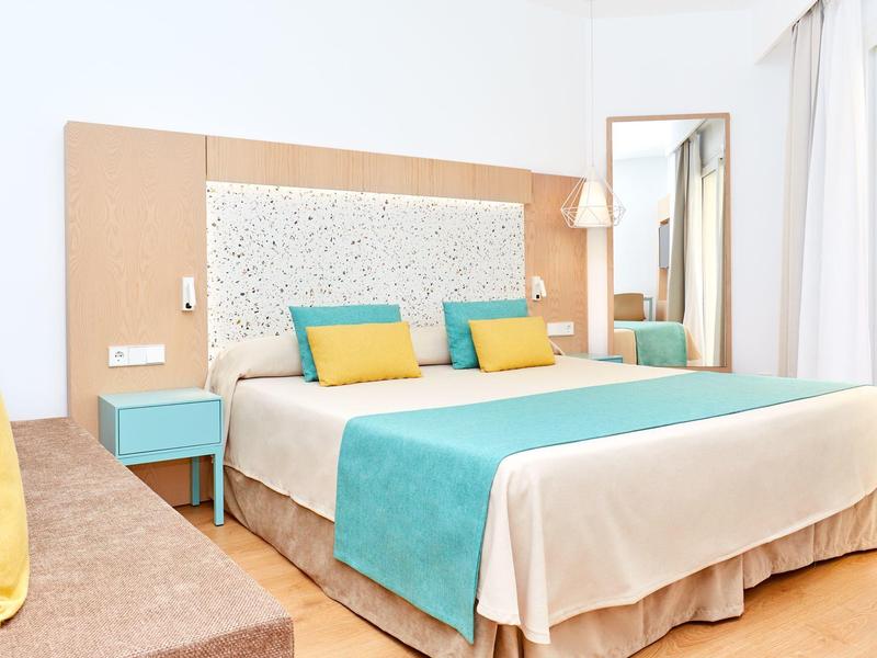 Camera d'hotel moderna con letto matrimoniale, accenti turchesi e gialli, dettagli in legno chiaro.