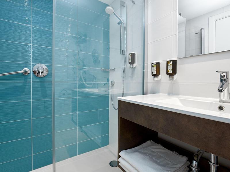Bagno moderno con doccia in vetro, piastrelle blu e lavabo ampio.