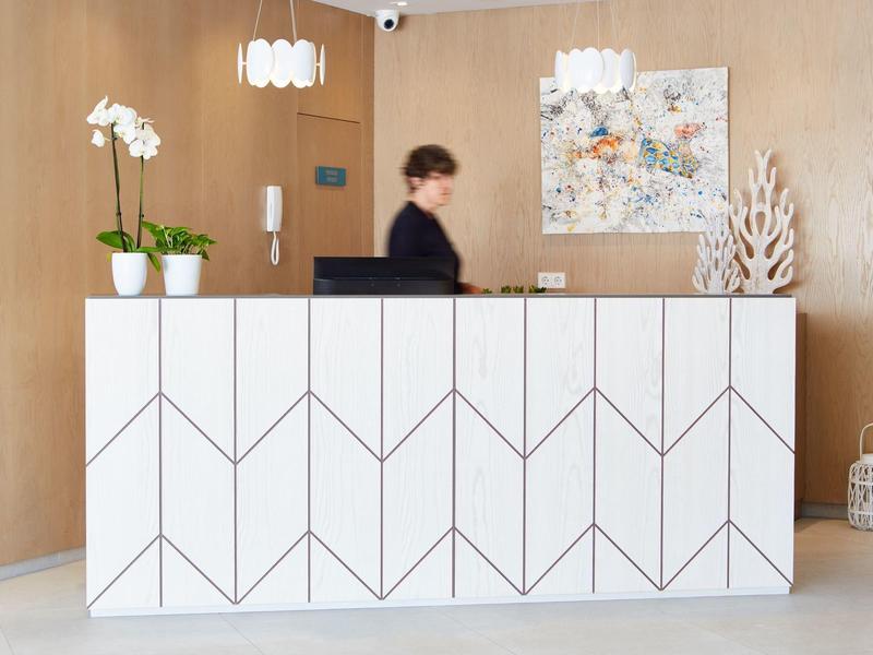 Reception d'hotel moderna con banco bianco geometrico, orchidee ed elementi decorativi.