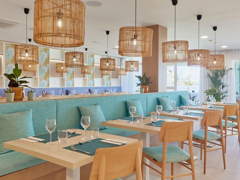 Ristorante luminoso con mobili in legno, cuscini blu e lampade di bambù sospese.