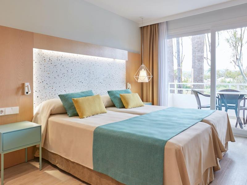 Camera d'hotel luminosa con letto matrimoniale, balcone e arredamento moderno e minimalista.