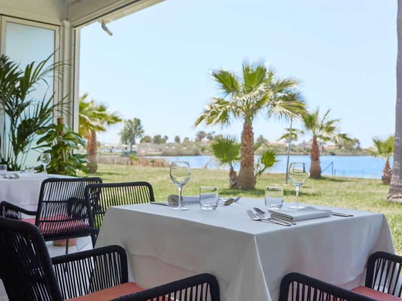 Terrazza con tavolo apparecchiato e vista su palme e acqua sullo sfondo.