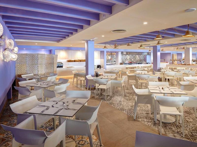 Duża nowoczesna restauracja z białymi stolikami i fioletowymi ścianami.