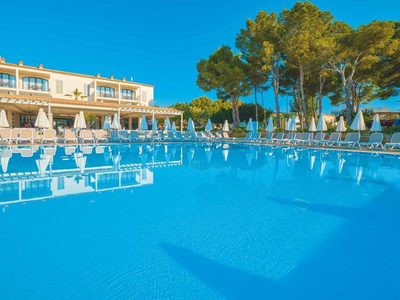 Przejrzysty basen na zewnątrz otoczony leżakami i parasolami, pod niebieskim niebem.