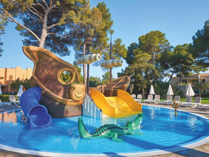 Mały basen z zjeżdżalnią w kształcie statku dla dzieci w słonecznym otoczeniu.