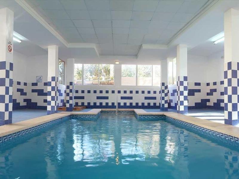 Jasny kryty basen z niebiesko-białymi kafelkami i leżakami.