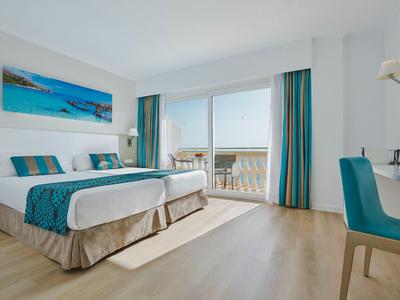 Jasny pokój hotelowy z łóżkiem podwójnym, balkonem i widokiem na morze.