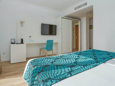 Nowoczesny pokój hotelowy z łóżkiem, biurkiem, niebieskim krzesłem i telewizorem na ścianie.