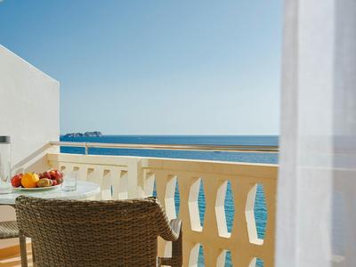 Balkon z wiklinowym krzesłem, talerz owoców i widokiem na morze pod niebieskim niebem.