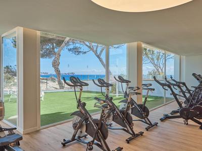 Siłownia z rowerami stacjonarnymi i dużymi oknami z widokiem na plażę i morze.