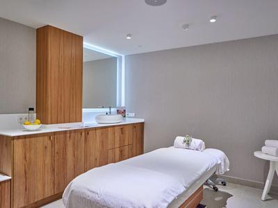 Jasne, nowoczesne pomieszczenie zabiegowe z łóżkiem do masażu i drewnianymi szafkami.