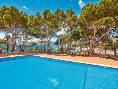 Duży basen z czystą wodą, otoczony drzewami, z widokiem na morze pod błękitnym niebem.