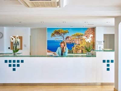 Nowoczesna recepcja hotelowa z białym kontuarem i muralem przedstawiającym letni krajobraz nad morzem.