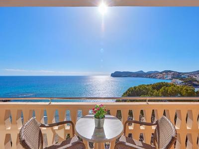 Balkon z stołem, krzesłami i kwiatami z widokiem na morze i słoneczne wybrzeże.