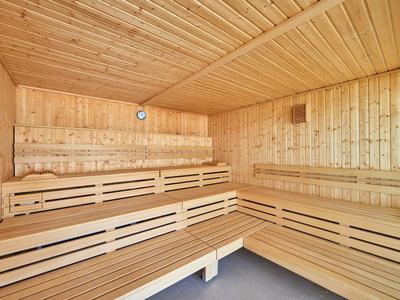 Drewniana sauna z wielopoziomowymi ławkami i skośnym sufitem z jasnego drewna.