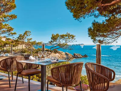 Taras z stołami i krzesłami z widokiem na morze i skały pod bezchmurnym niebem.